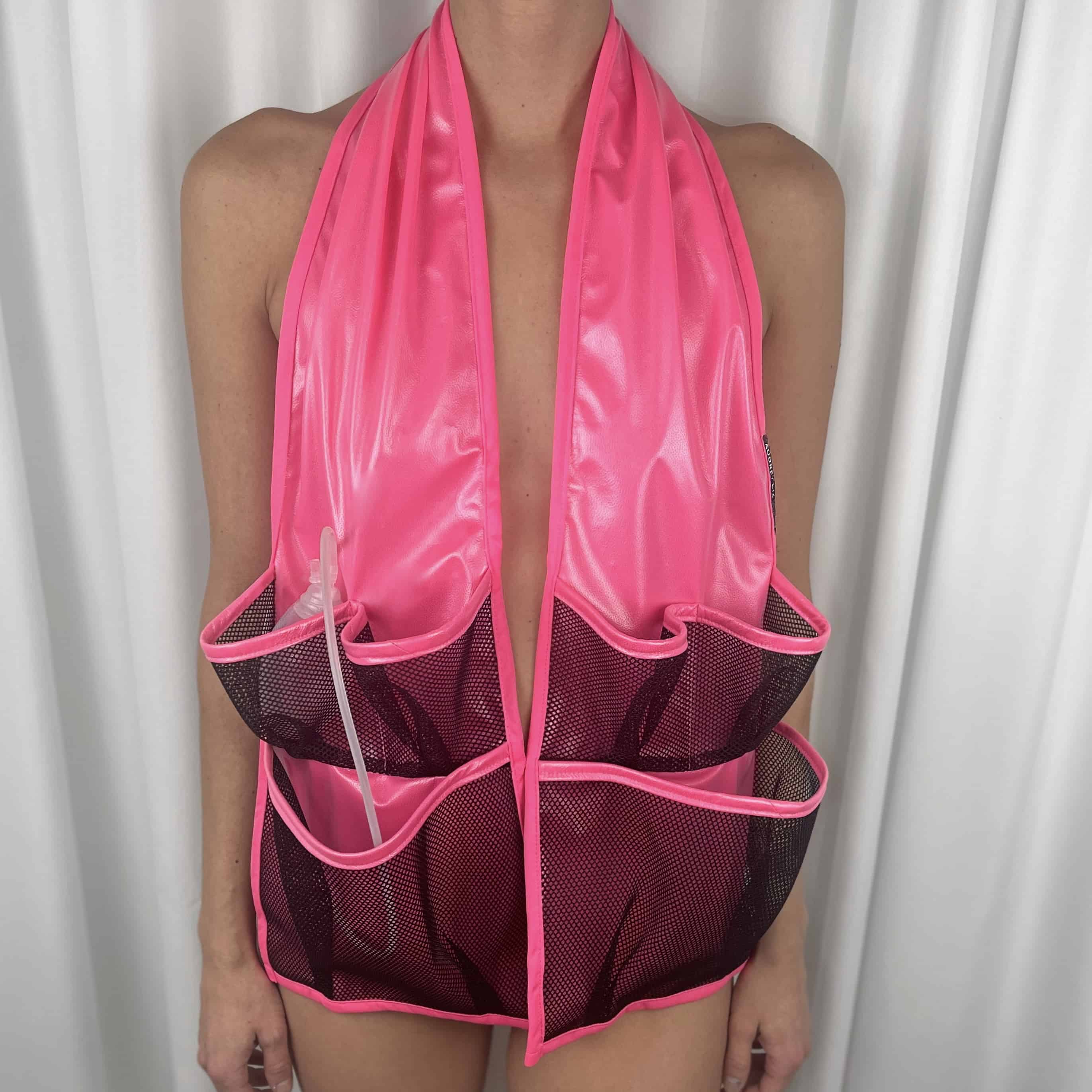 Body of woman wearing a bright pink waterproof scarf with mesh pockets. Post-surgery drains and tubing are placed in the pockets.