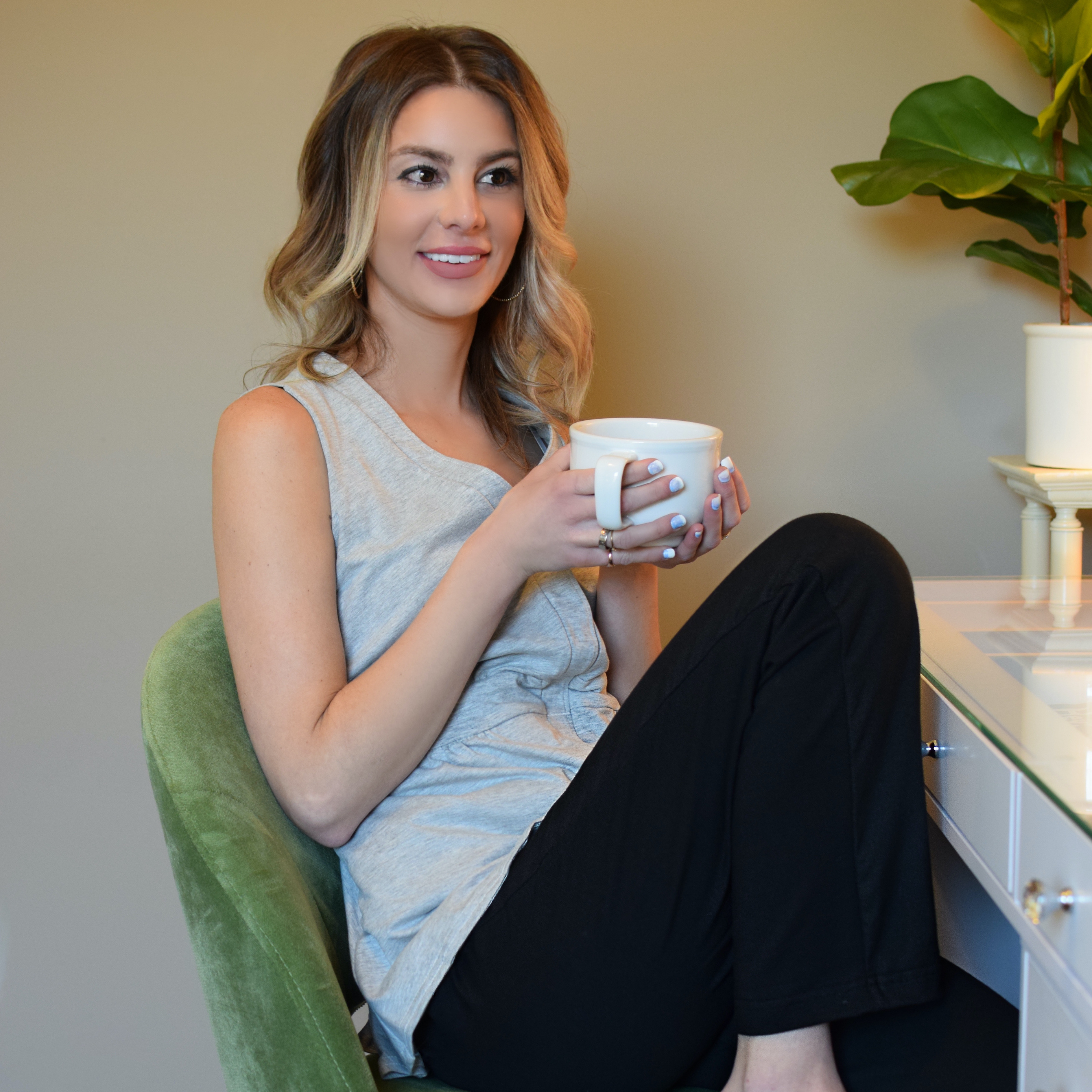 Woman lounging wearing a grey mastectomy top and black elastic waist pants, holding a cup of coffee.