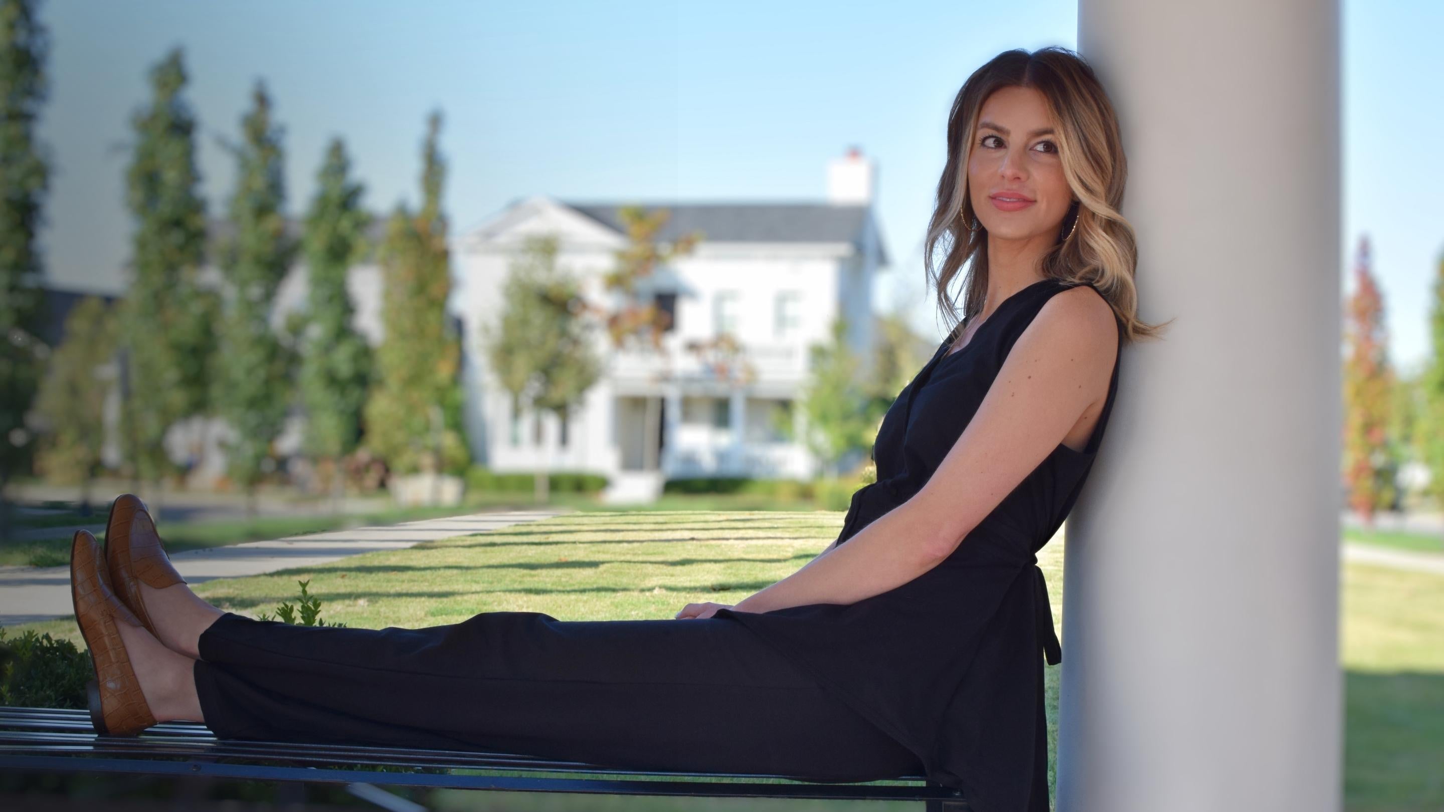 Model sitting on a bench looking to the side wearing a black mastectomy shirt with matching black pants.