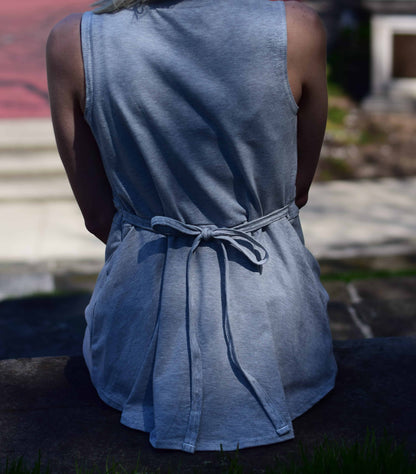 Woman in a grey sleeveless mastectomy shirt with a bow tied in back, sitting outdoors.
