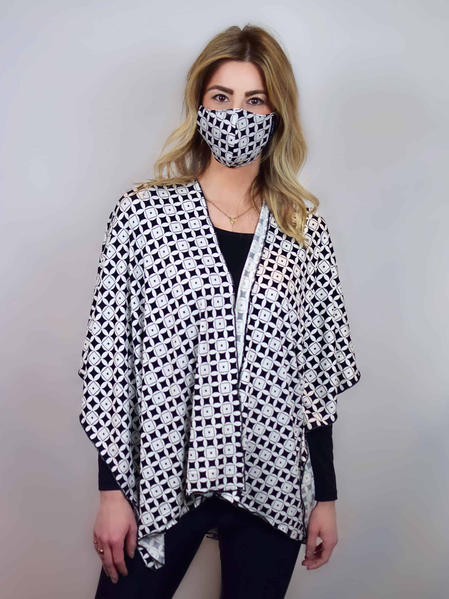 Woman wearing a black and white patterned face mask, with a shawl in the same pattern, draped over both shoulders.